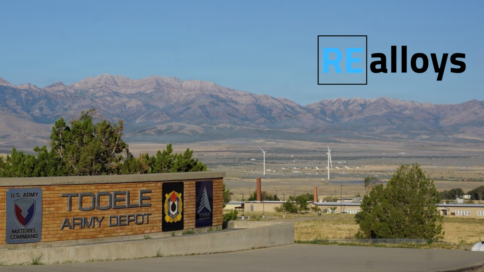 Sign reads 'TOOLE ARMY DEPOT' with U.S. Army Materiel Command badge; desert landscape and mountains in the background, and a blue REalloys logo in the sky.