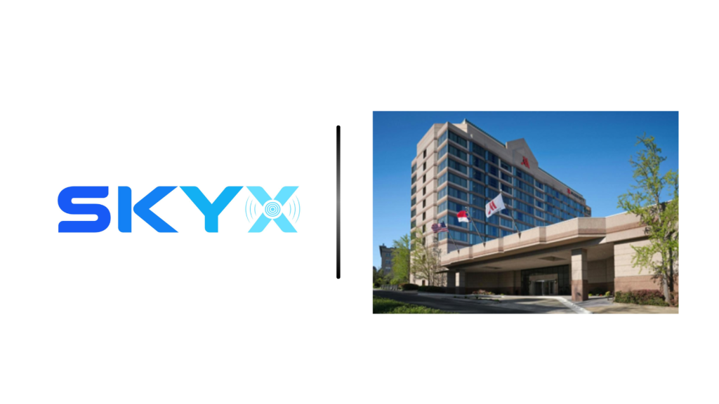 SKYX logo on the left separated by a vertical divider from a modern hotel building on the right, with flags at the entrance.