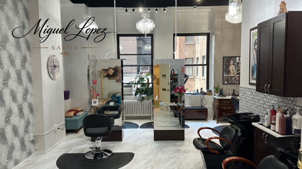 Elegant hair salon interior with black styling chairs, large mirrors, chandeliers, and a windowed reception area.