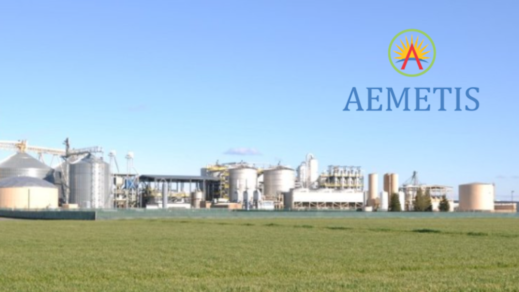 Industrial plant skyline with silos and machinery; AEMETIS logo in the upper-right corner.